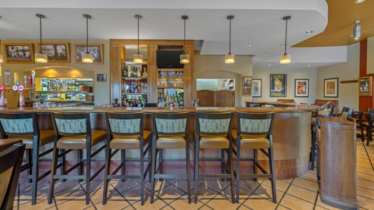 Full-service hotel bar and lounge with seating, liquor shelves, and restaurant kitchen access.