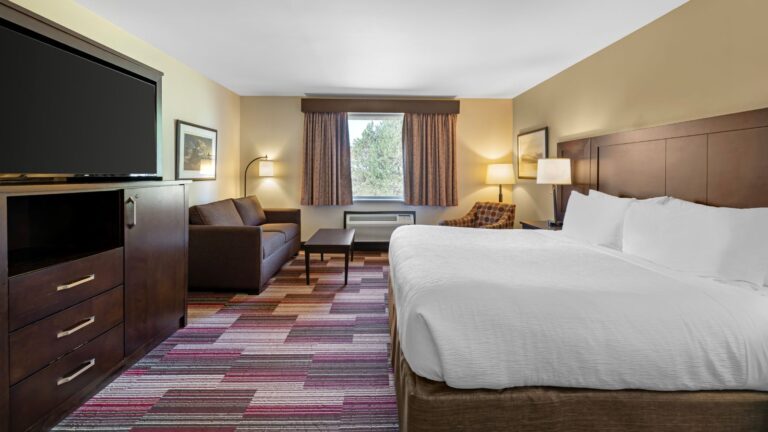 King bed hotel room with sofa and TV cabinet, and large window.